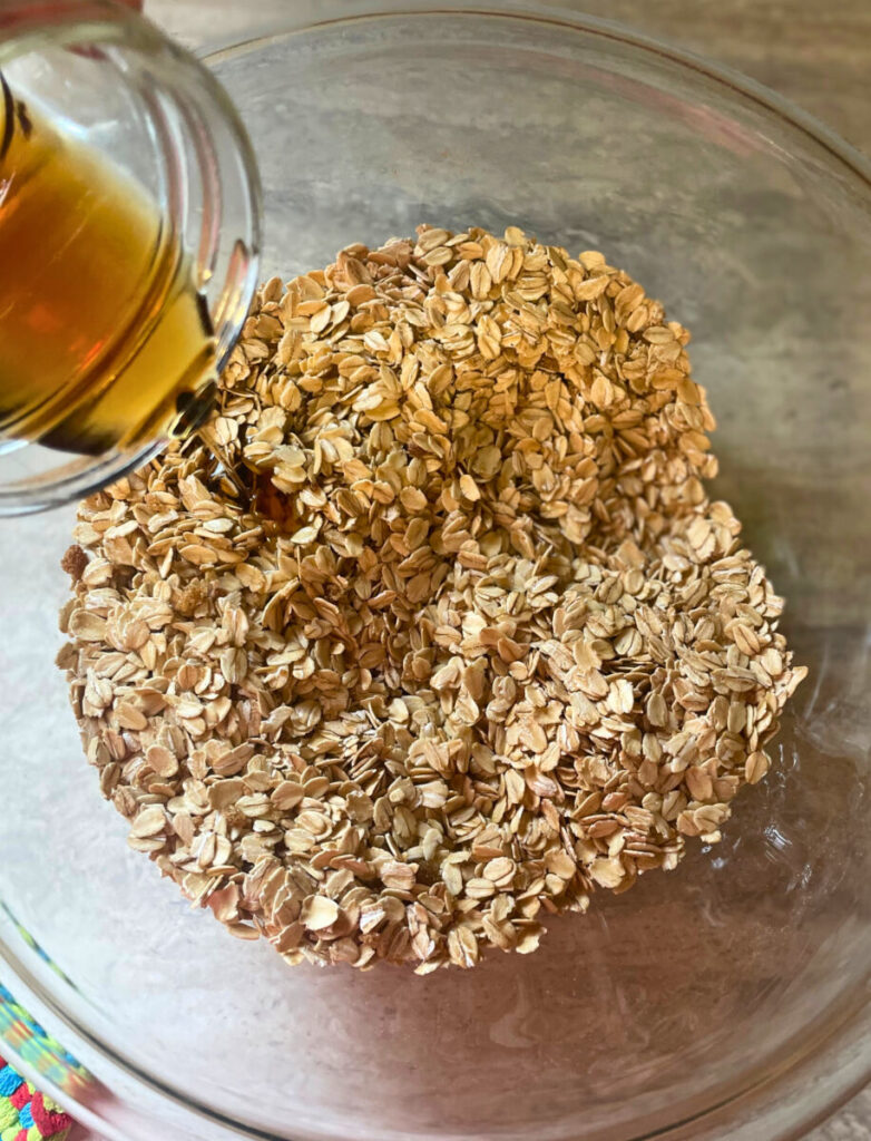 maple syrup being poured into a bowl of oats and dry ingredients