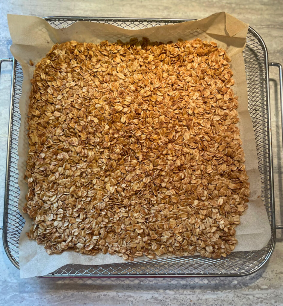 baked granola spread out on an air fryer tray