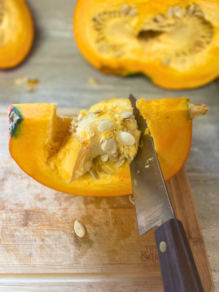 pulp and seeds of a pumpkin being scraped out with a knife