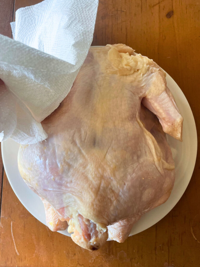 whole chicken being dried with a paper towel