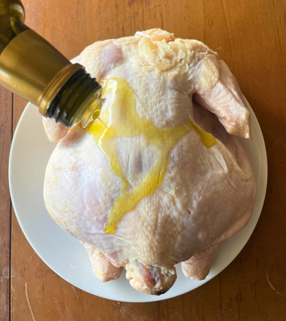 olive oil being poured on a whole raw chicken